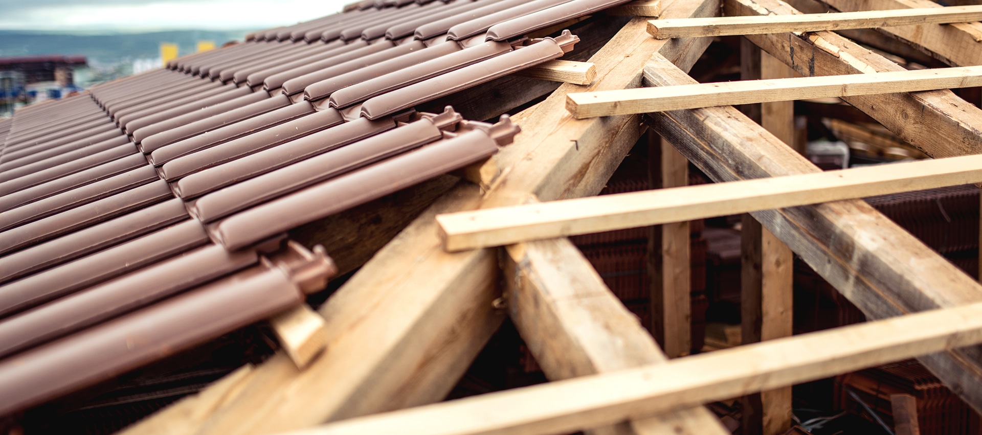 Toiture en construction, avec tuiles marron brillantes posées et charpente en bois apparente.