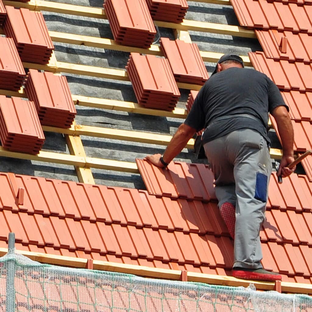 Couvreur installe des tuiles de toit : Pose rapide et efficace. Couvreur installant des tuiles de toit en terre cuite. L'homme en t-shirt noir pose les tuiles sur l'armature en bois.