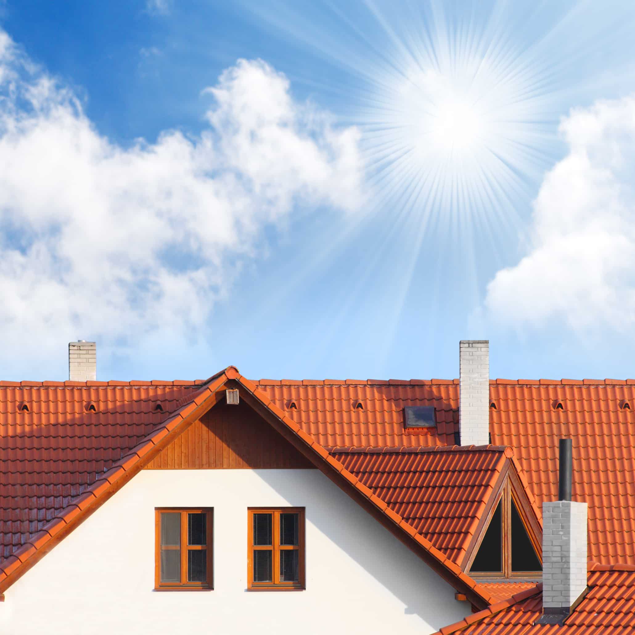 Toit en tuiles rouges de maison : soleil, ciel bleu et nuages. Toit en tuiles rouges avec cheminées et fenêtres, sous un ciel bleu éclatant, soleil rayonnant et nuages blancs.